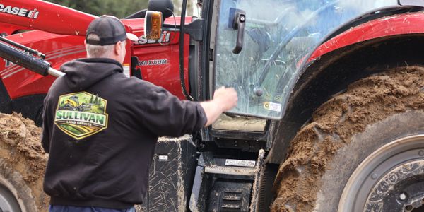 Man cleaning mud off a red tractor's window.