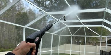 Person using a pressure washer to clean a screened enclosure.