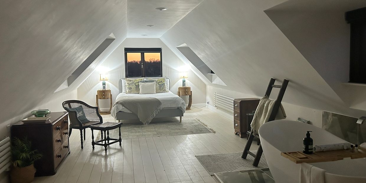 Cozy attic bedroom with a bed, vintage furniture, and a freestanding bathtub.