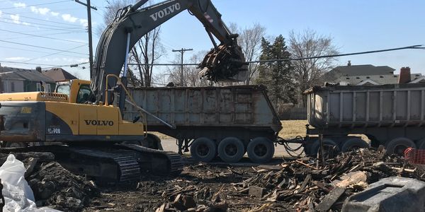 Excavator loading debris into a dump truck at a demolition site.
