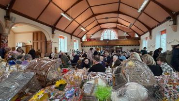 Community gathering in a hall with gift baskets.