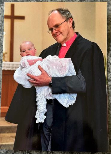 Clergyman holding a baby during a ceremony.