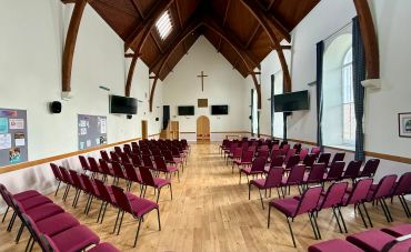 Empty church hall with rows of red chairs.