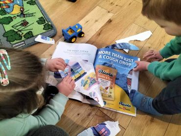 Two children looking at torn magazine pages on the floor.