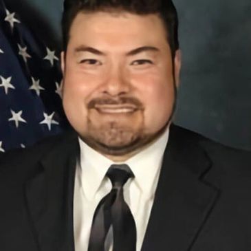 Man in a suit smiling in front of an American flag.