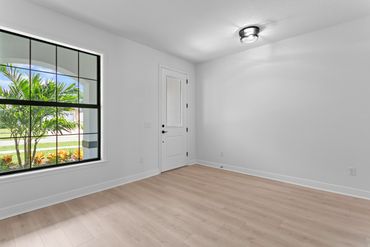 Empty room with light wood flooring and large window showing outdoor greenery.