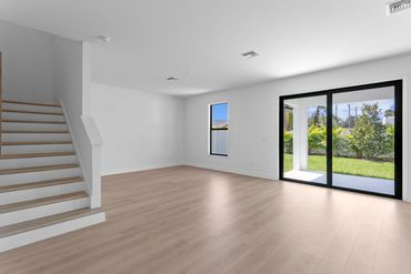 Empty modern living room with wooden floors and large sliding glass door.