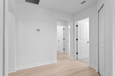 Bright hallway with white walls and light wood flooring leading to open doors.
