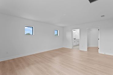 Empty room with light wood flooring and white walls with two small windows.