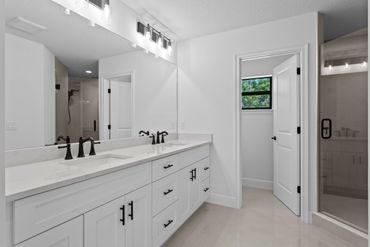 Modern white bathroom with dual sinks and a glass shower.