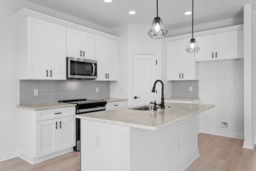 Modern white kitchen with marble countertops and black fixtures.