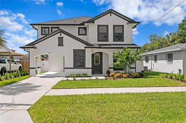 Modern two-story house with a clean front yard and driveway under a blue sky.