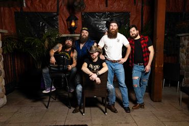 A group of five bearded men posing in a rustic indoor setting.