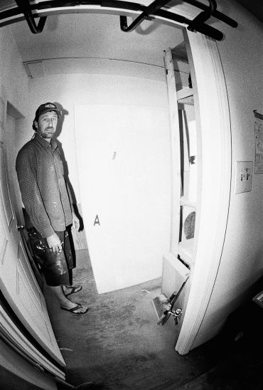 Man standing in a narrow room with a white door and tools.