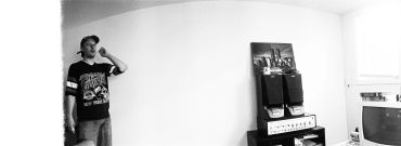 Man drinking in a sparse room with vintage electronics.