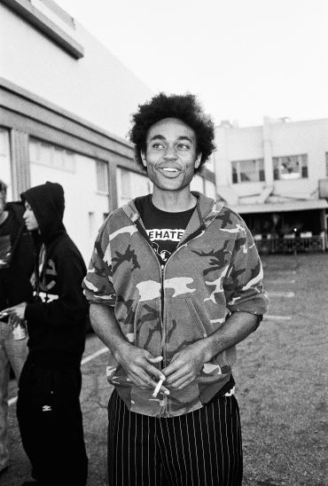 Young man smiling casually outdoors with a cigarette.