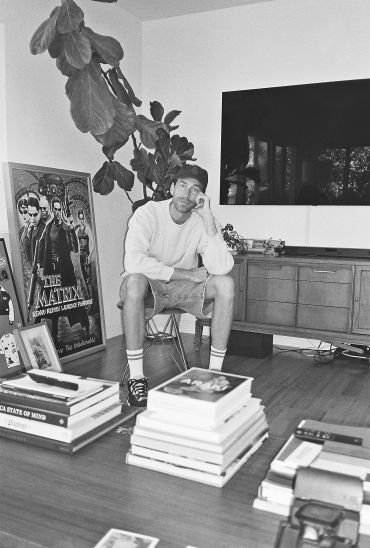 Man sitting in a living room surrounded by books and posters.