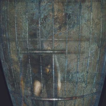 A person trapped inside a rusty metal cage with a distressed expression.