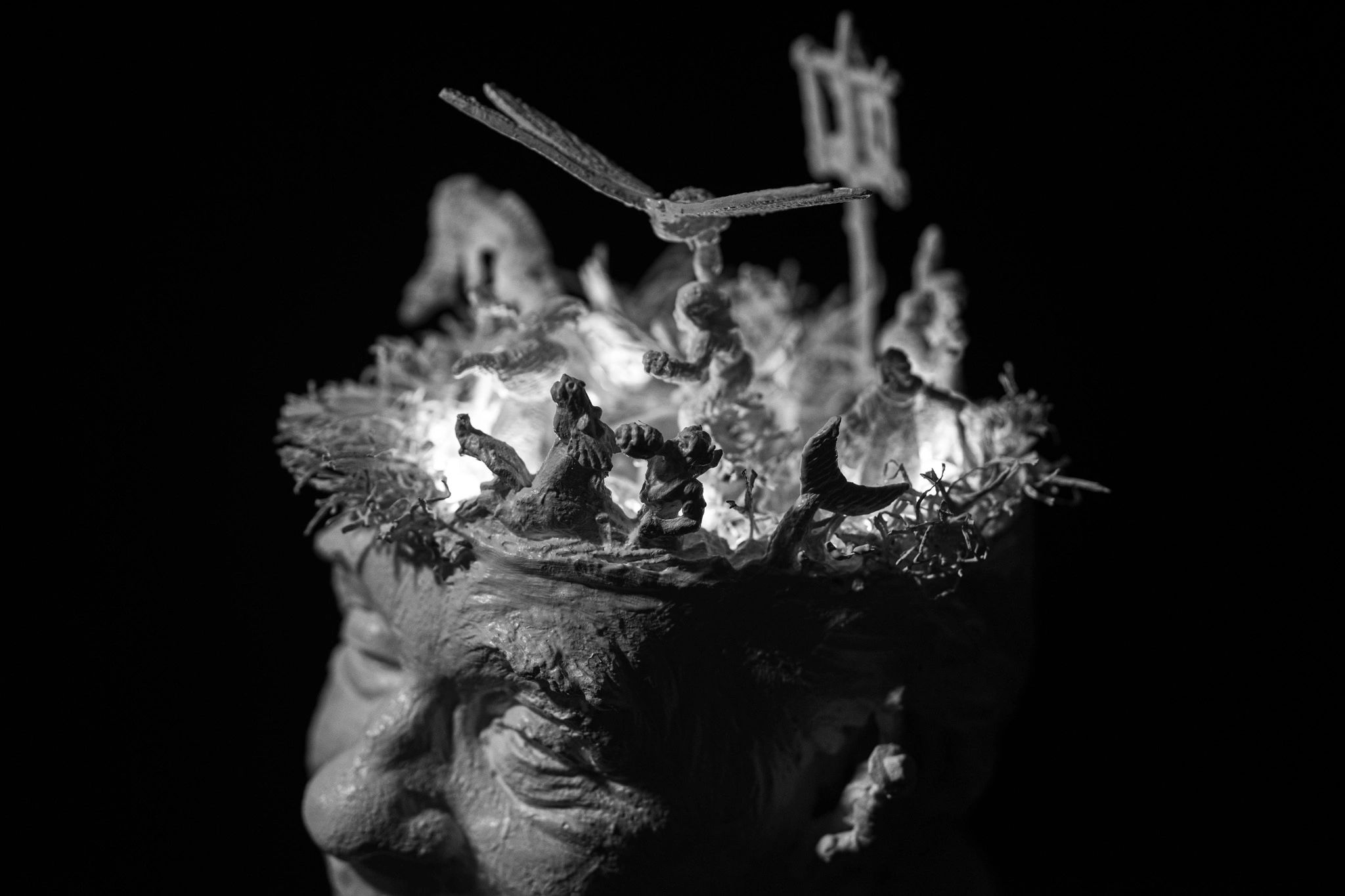 Intricate sculpture with mythical figures and a dragonfly on a head.