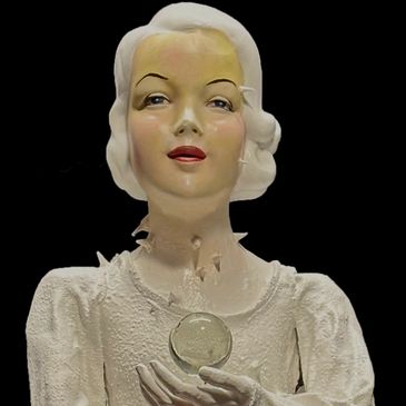Vintage mannequin with white hair holding a glass orb against a black background.