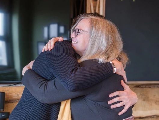 Two people warmly embracing, smiling as they share a supportive hug, 