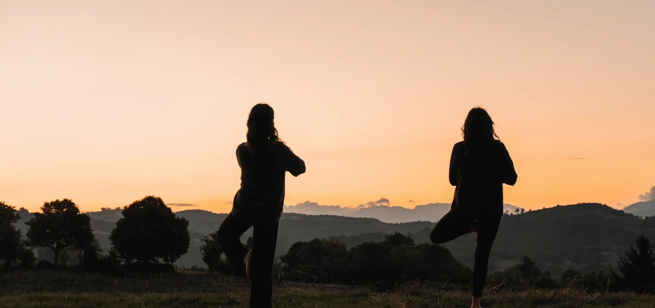 Deux personnes en silhouette faisant du yoga au coucher du soleil.