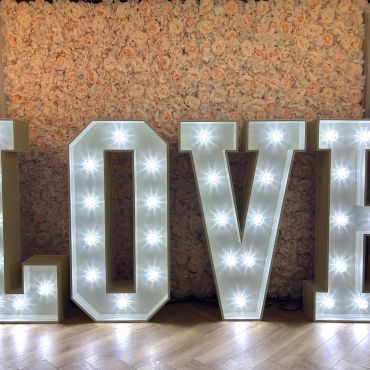 Illuminated LOVE letters with floral backdrop on wooden floor.