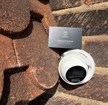 White security camera mounted on a brick wall beside a business card.