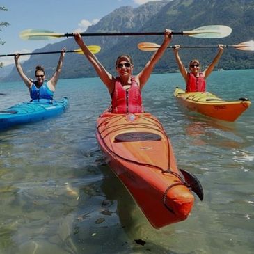 Three people kayaking joyfully on a clear lake with mountains in the background.