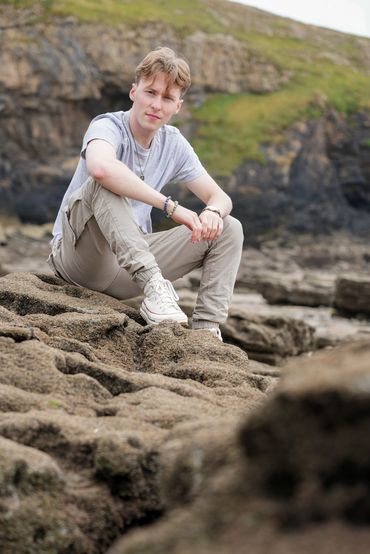Jamie Moreland sat on rocks with cliffs in the background on Southerndown Beach in Wales