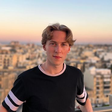 Jamie Moreland stood on a rooftop balcony with a sunset background in Malta