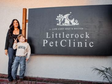 A woman and child stand smiling by a Littlerock Pet Clinic sign.