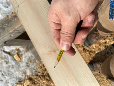 Hand holding a small yellow pencil over wood.