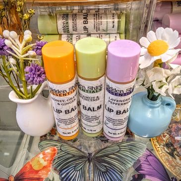 Three lip balms - orange, green and purple sitting on a glass counter surrounded by flowers