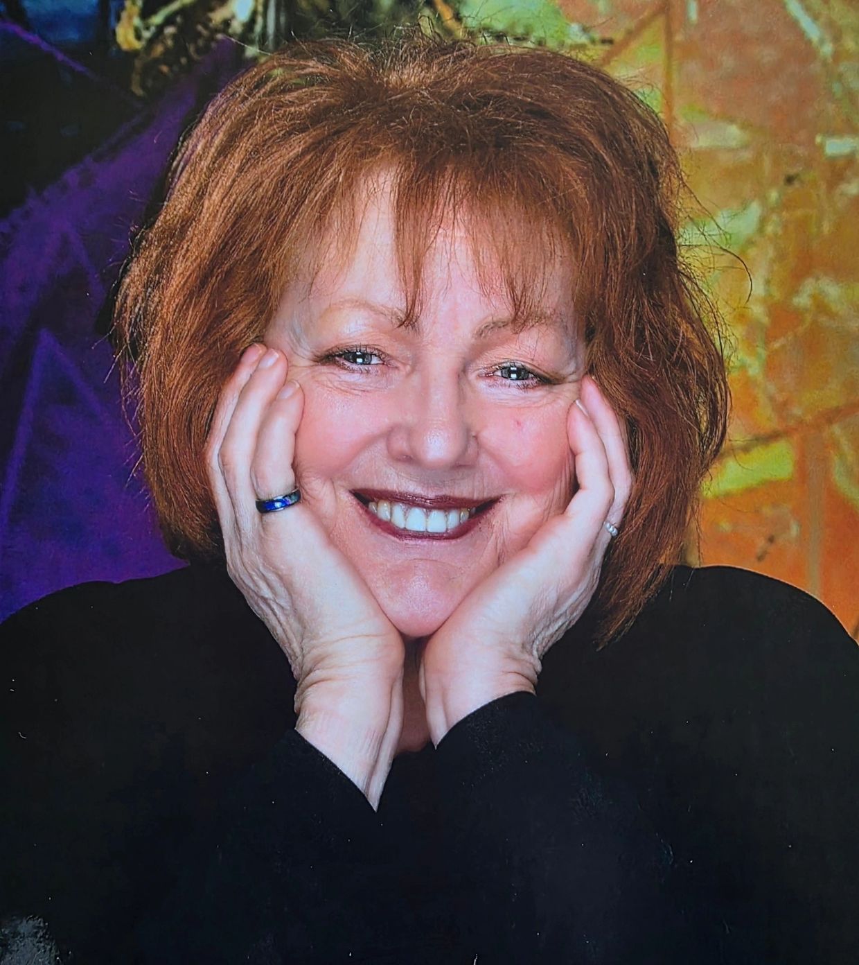 Smiling woman with red hair resting her face in her hands.