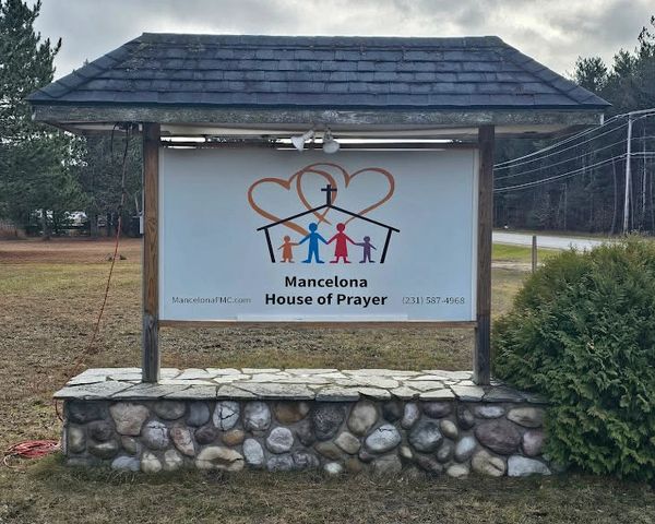 Sign for Mancelona House of Prayer with family and cross illustration.