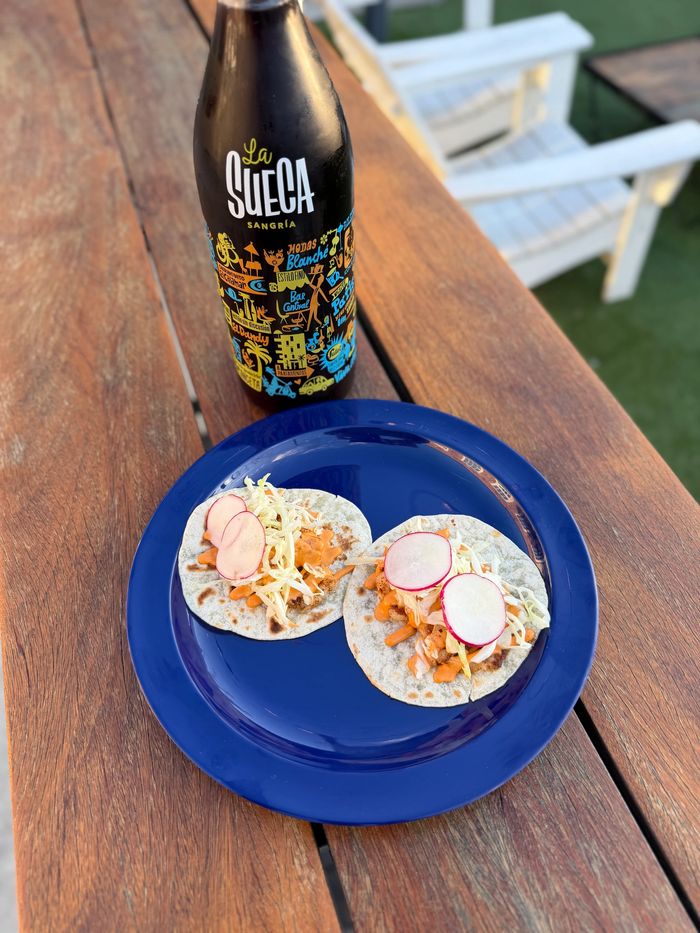 Two Blackened Shrimp tacos with radish and chili crema on a blue plate with a sangria bottle on a wooden table.