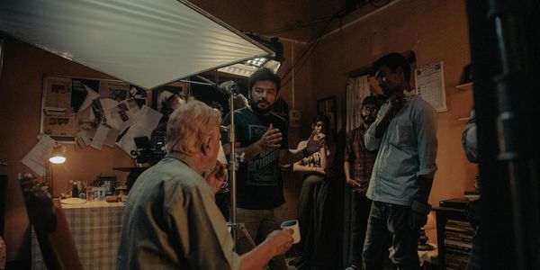 Film crew directs an elderly actor in a dimly lit room.