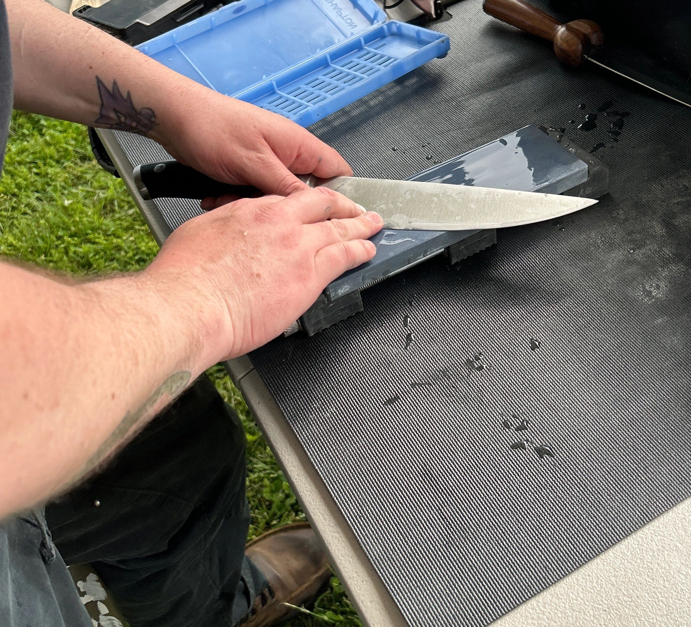 Person sharpening a large knife on a whetstone outdoors.