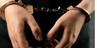 Hands in metal handcuffs against black background.