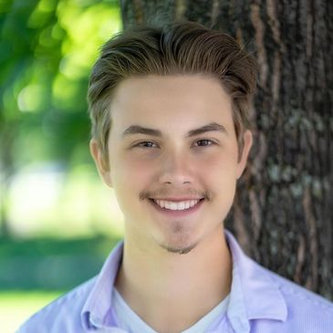 Young man smiling outdoors by a tree.