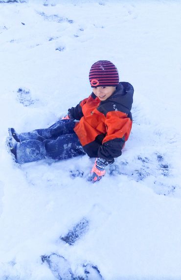 Child sitting in the snow with a striped hat and orange jacket.