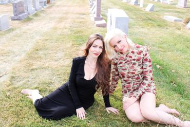 Two women sitting on grass in a cemetery.