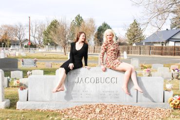 Two women sitting barefoot on a gravestone in a cemetery.