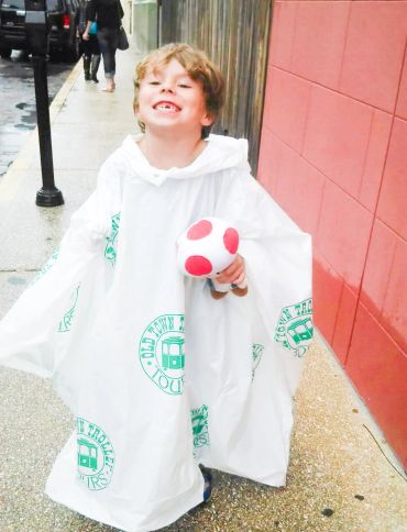 Smiling child in a white rain poncho holding a red and white mushroom toy.