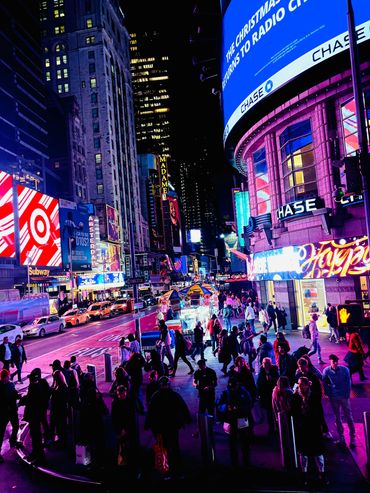 Nighttime city street filled with people and bright billboards.
