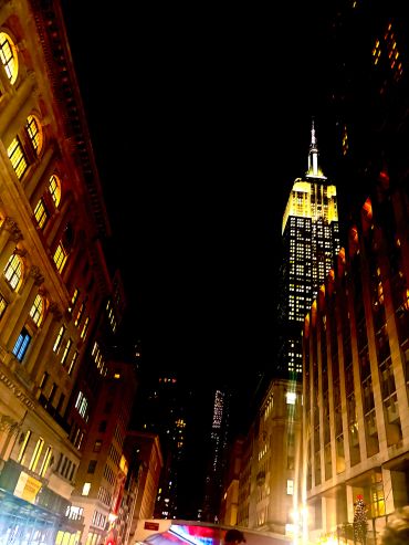 Night view of a city street with lit buildings.