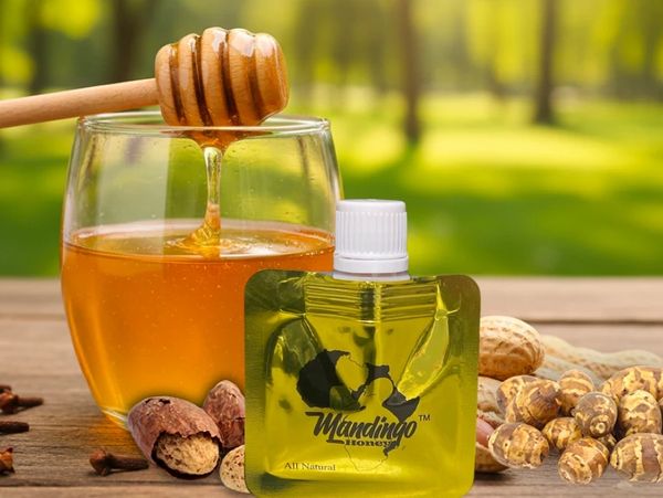 Glass of honey with honey dipper, nuts, and Mandingo Honey pouch on wooden surface.