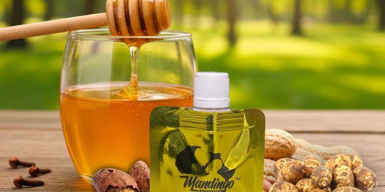 Glass of honey with honey dipper, nuts, and Mandingo Honey pouch on wooden surface.