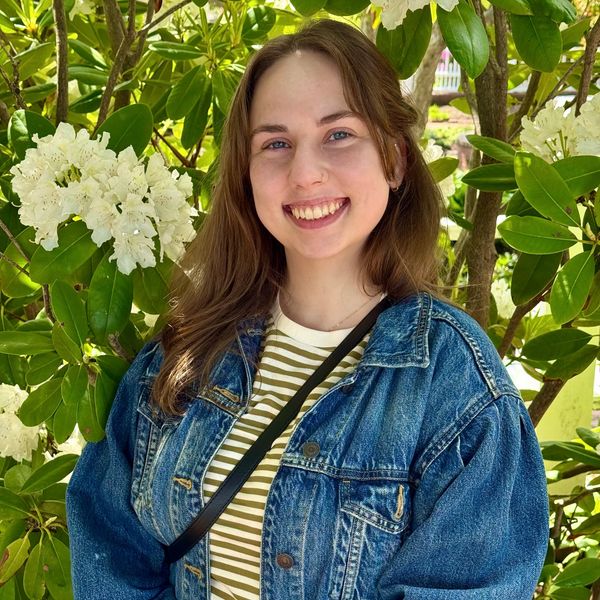 Woman with Brown hair smiling in front of flowers. 